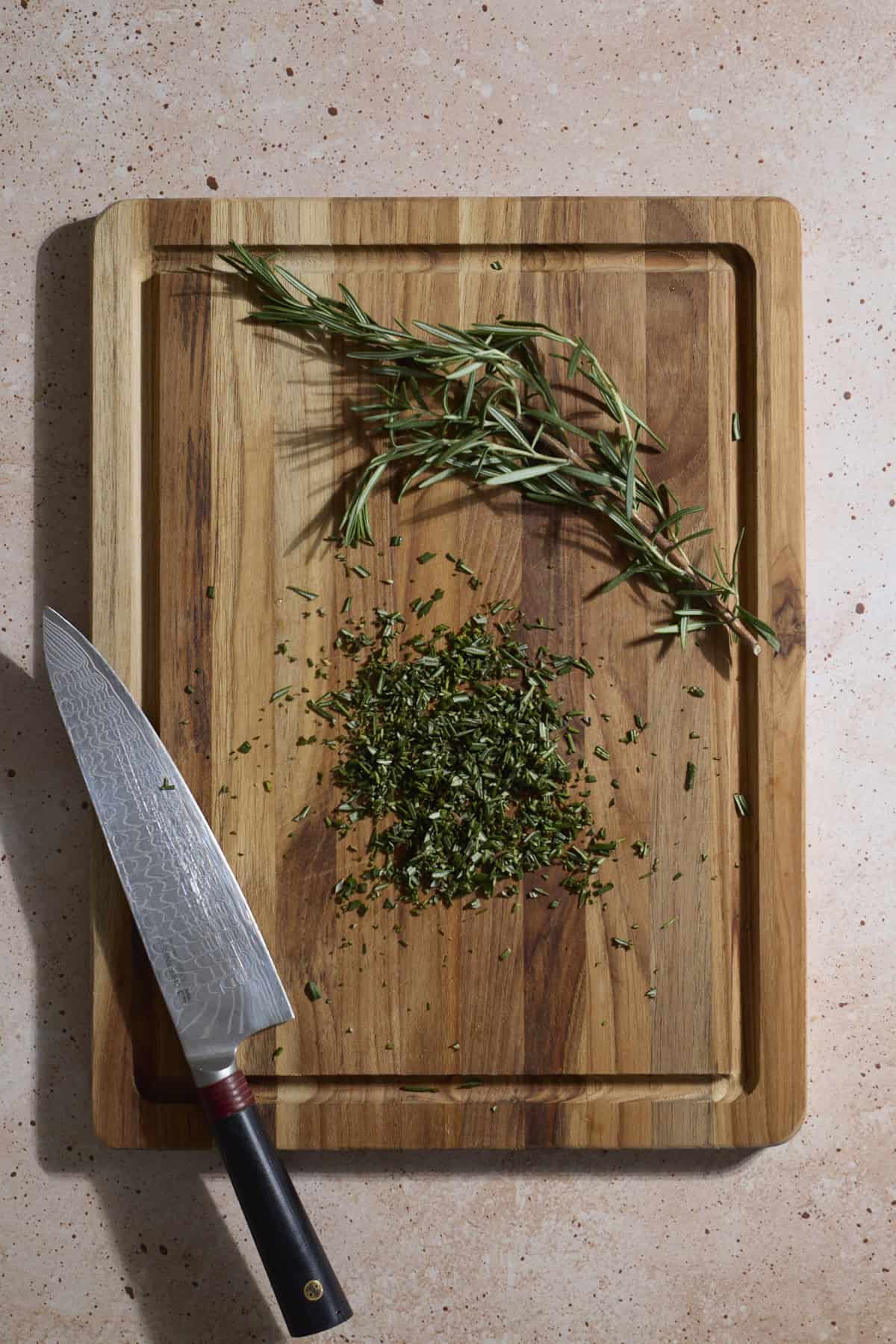 Rosemary chopped on a wooden cutting board.
