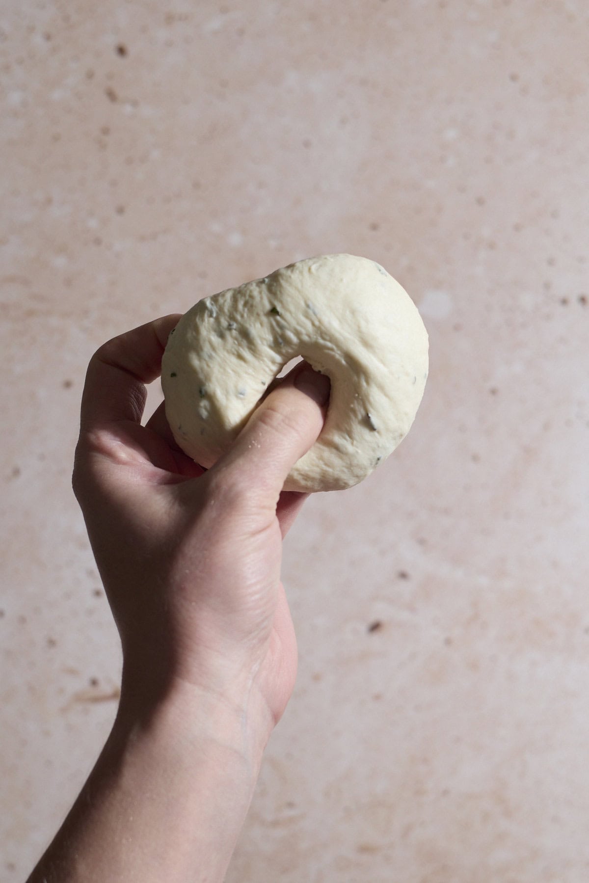 A thumb pressing the hole into the center of a bagel.