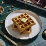 Syrup pouring onto a stack of Sourdough Sweet Potato Waffles.