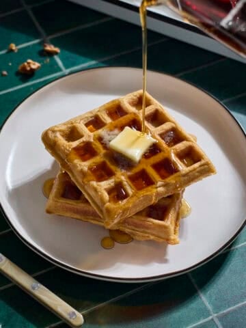 Syrup pouring onto a stack of Sourdough Sweet Potato Waffles.