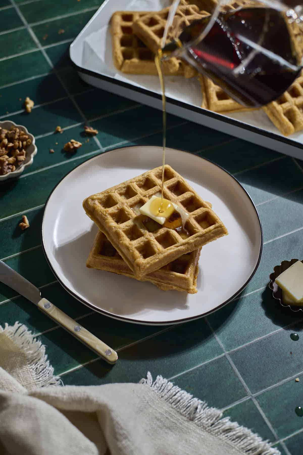 Syrup pouring onto a stack of Sourdough Sweet Potato Waffles.