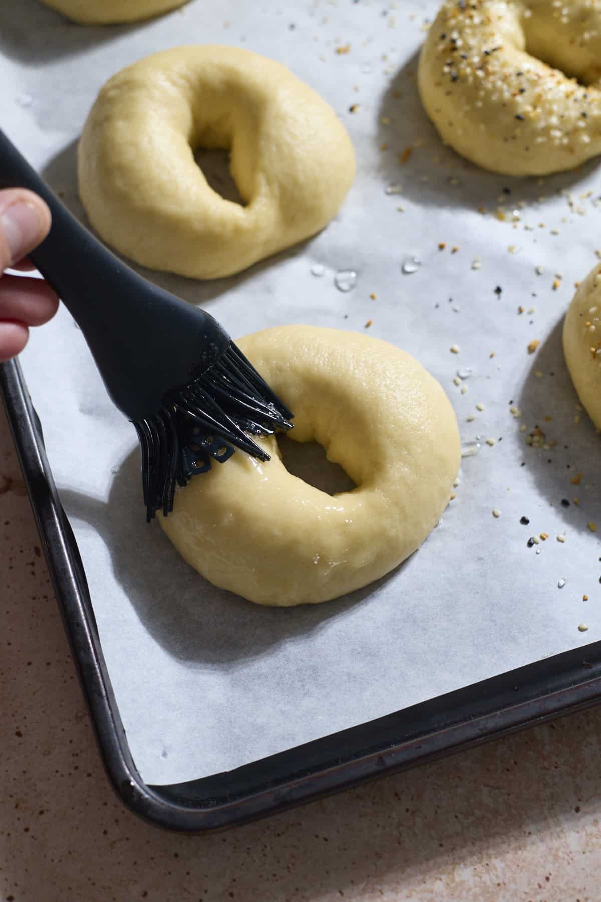 A brush putting egg wash on each bagel.