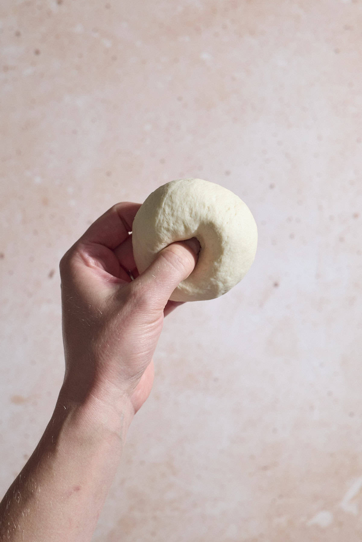 A thumb pressing a hole in the center of the bagel.