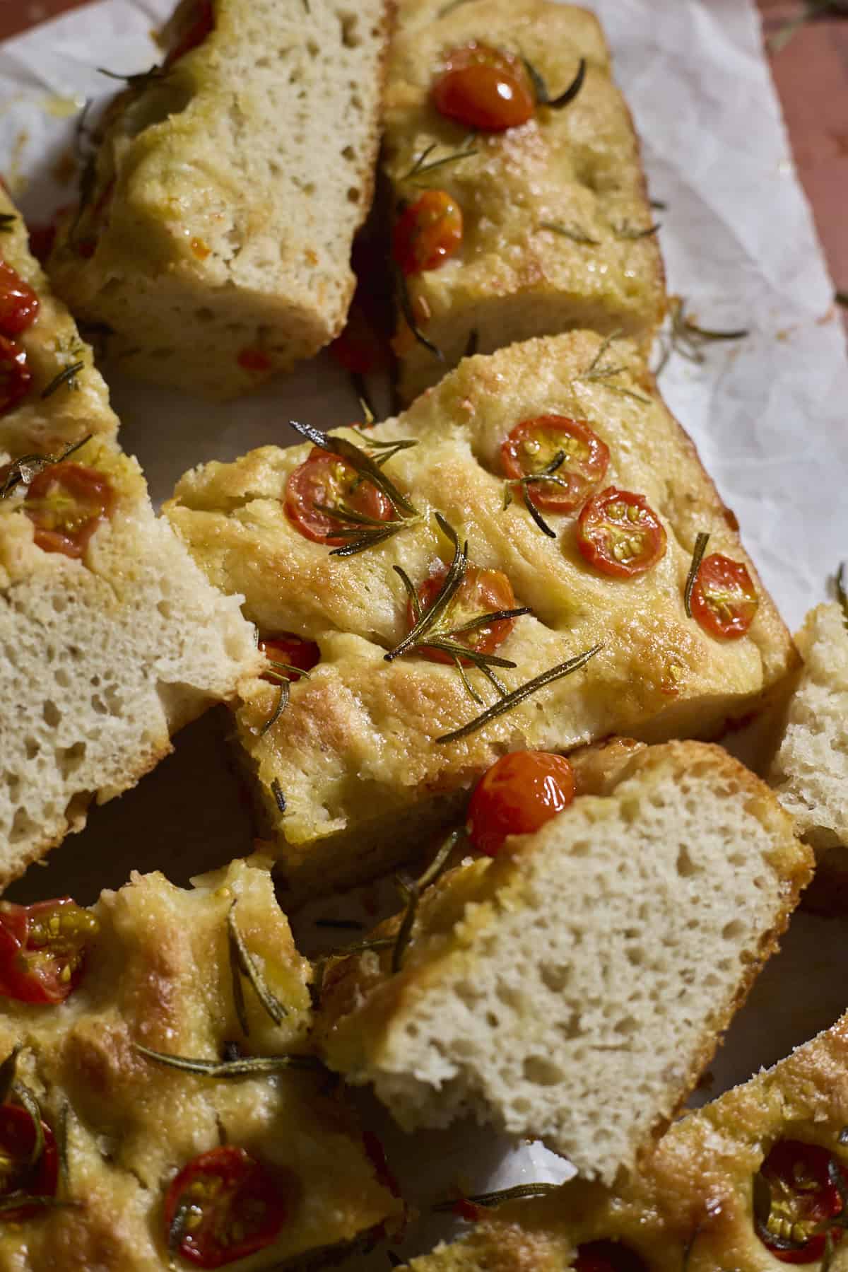 Slices of focaccia topped with cherry tomatoes on white parchment paper.