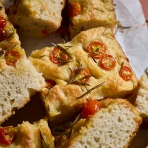 Slices of focaccia topped with cherry tomatoes on white parchment paper.