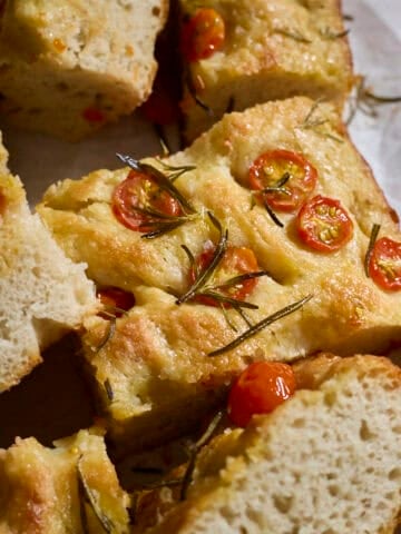 Slices of focaccia topped with cherry tomatoes on white parchment paper.