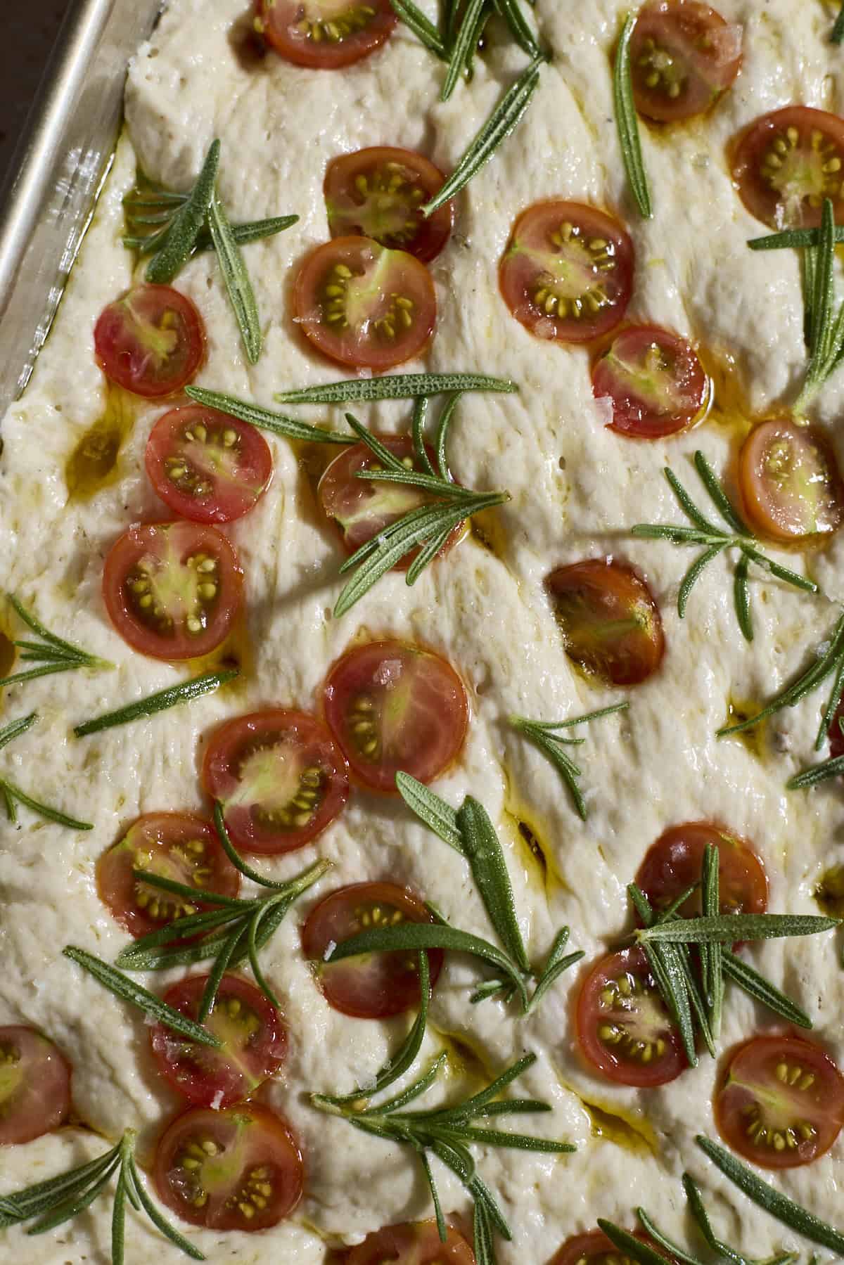 Dough topped with halved cherry tomatoes and rosemary sprigs.
