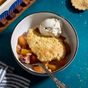 Sourdough Peach Cobbler in a bowl with a scoop of vanilla ice cream.