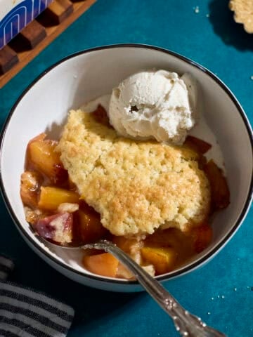 Sourdough Peach Cobbler in a bowl with a scoop of vanilla ice cream.