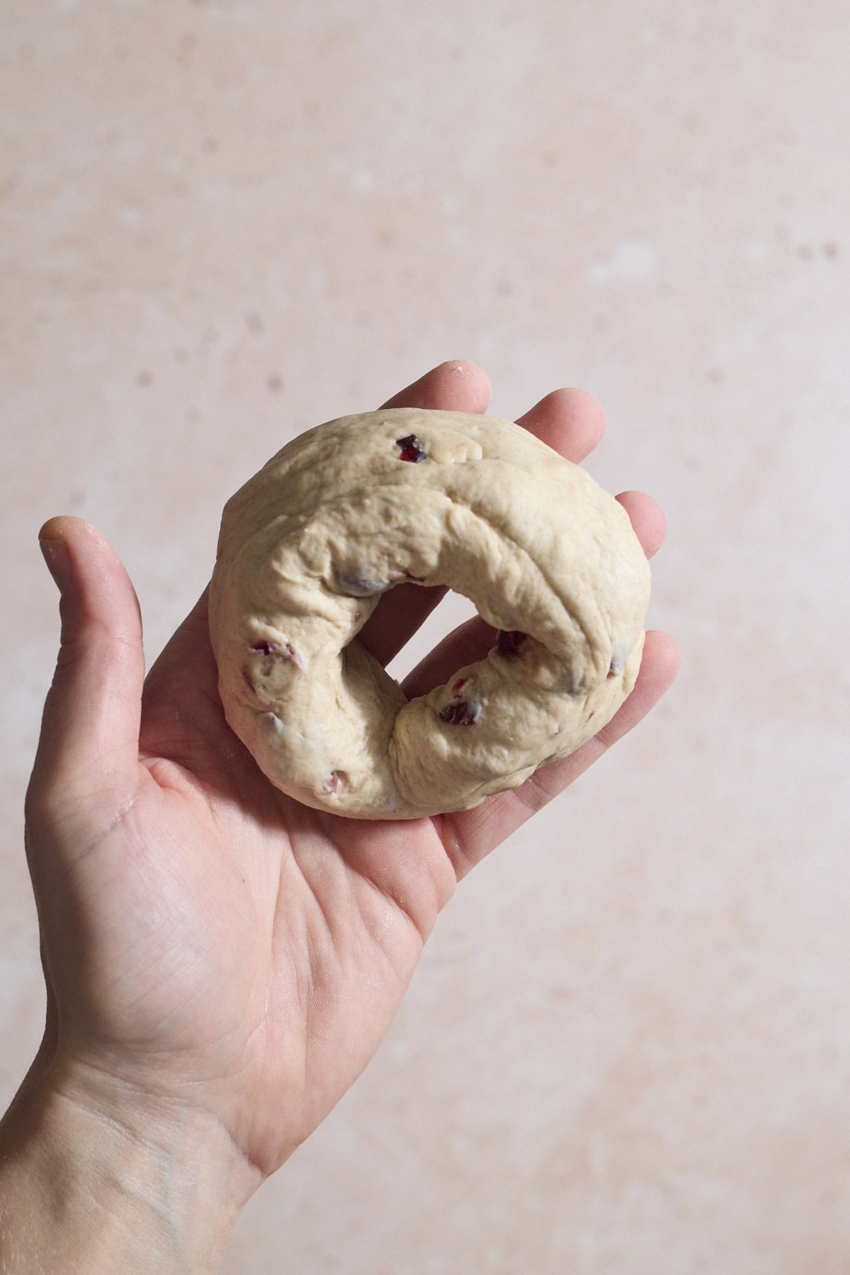 Dough shaped into a bagel in the palm of a hand.