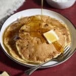 A stack of Sourdough Protein Pancakes with syrup pouring on top.