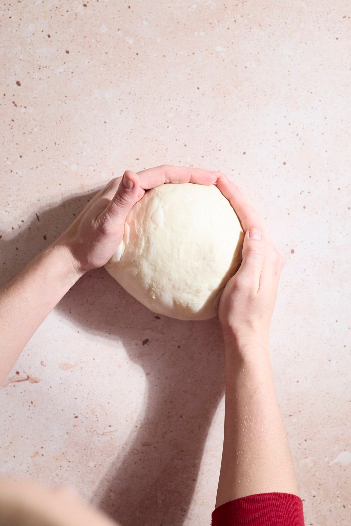 Hands cupping around the dough to shape the loaf.