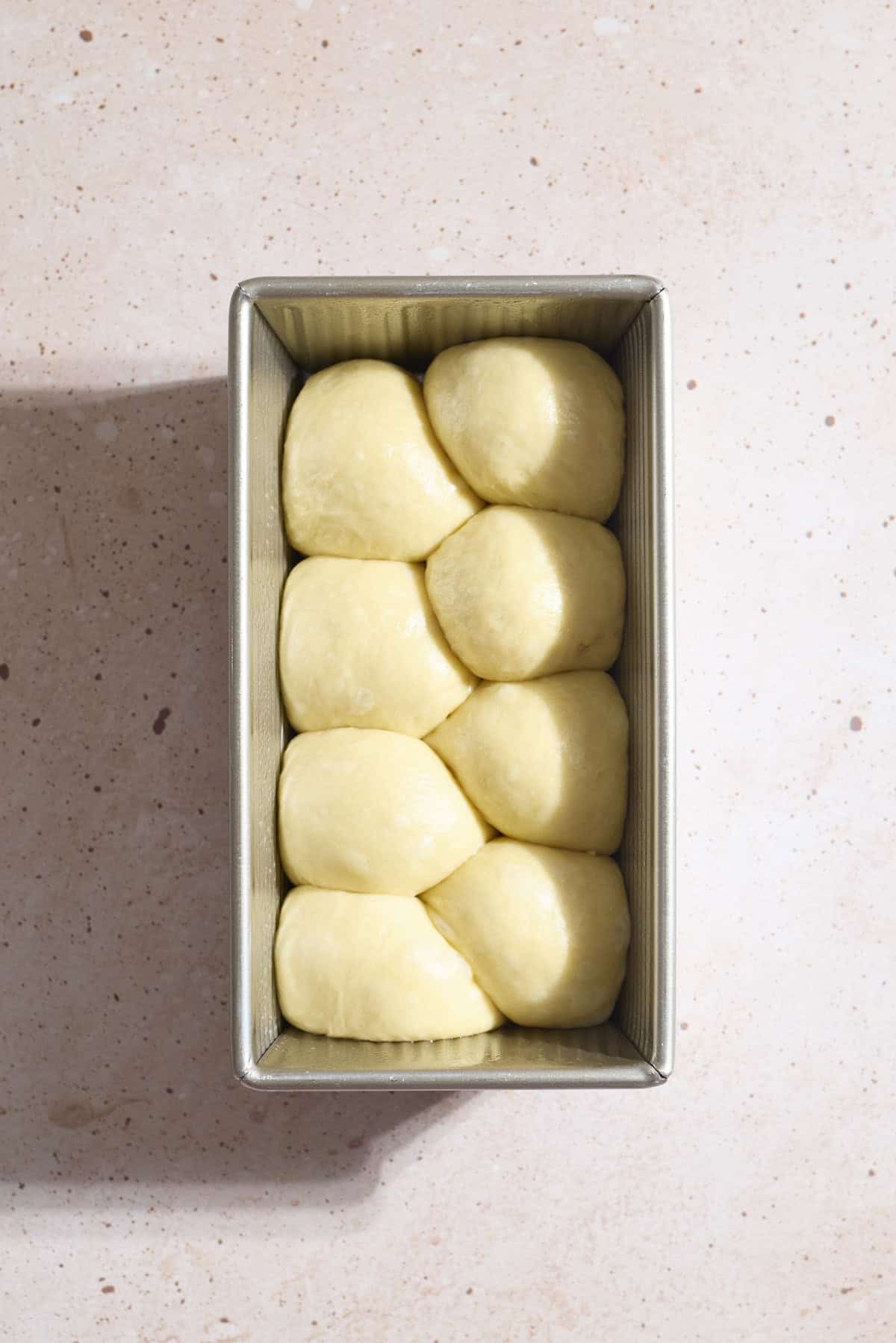 Eight dough rolls staggered in the baking pan.