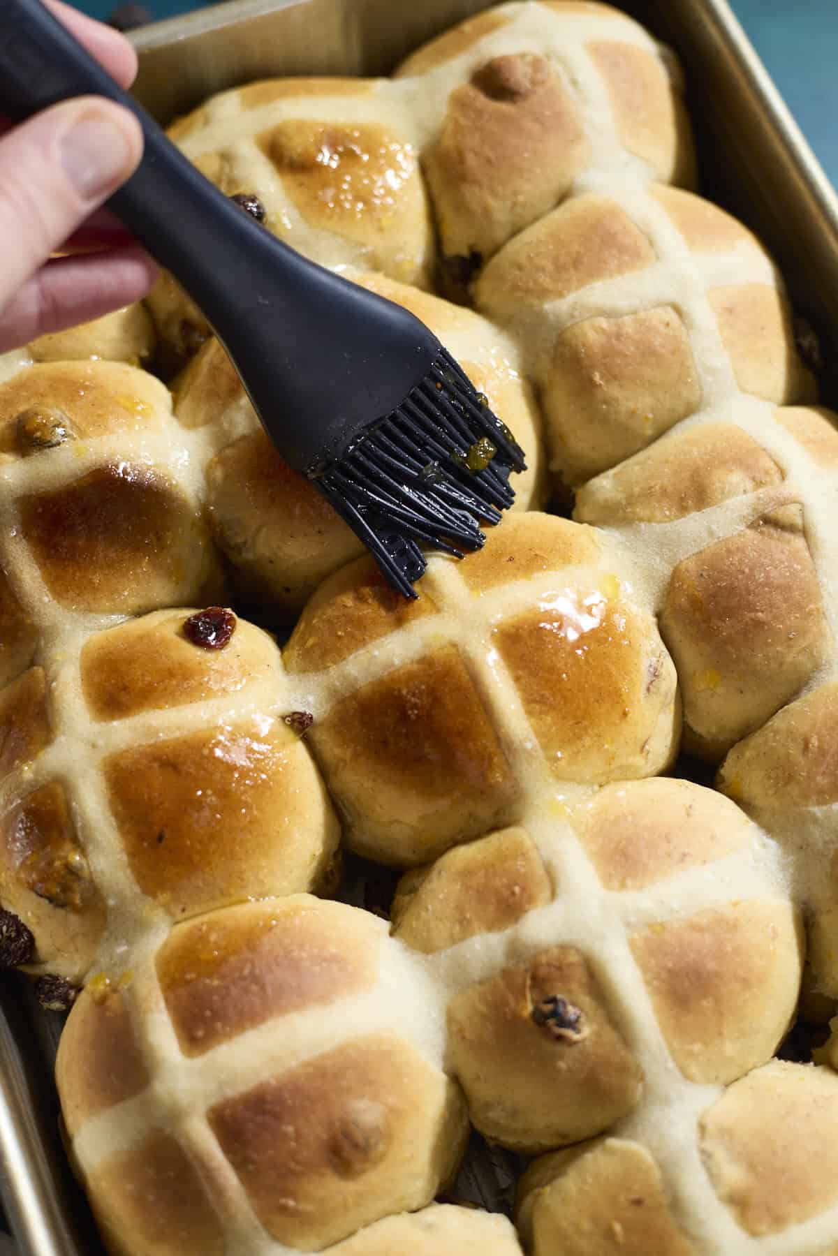 Buns being brushed with orange glaze.