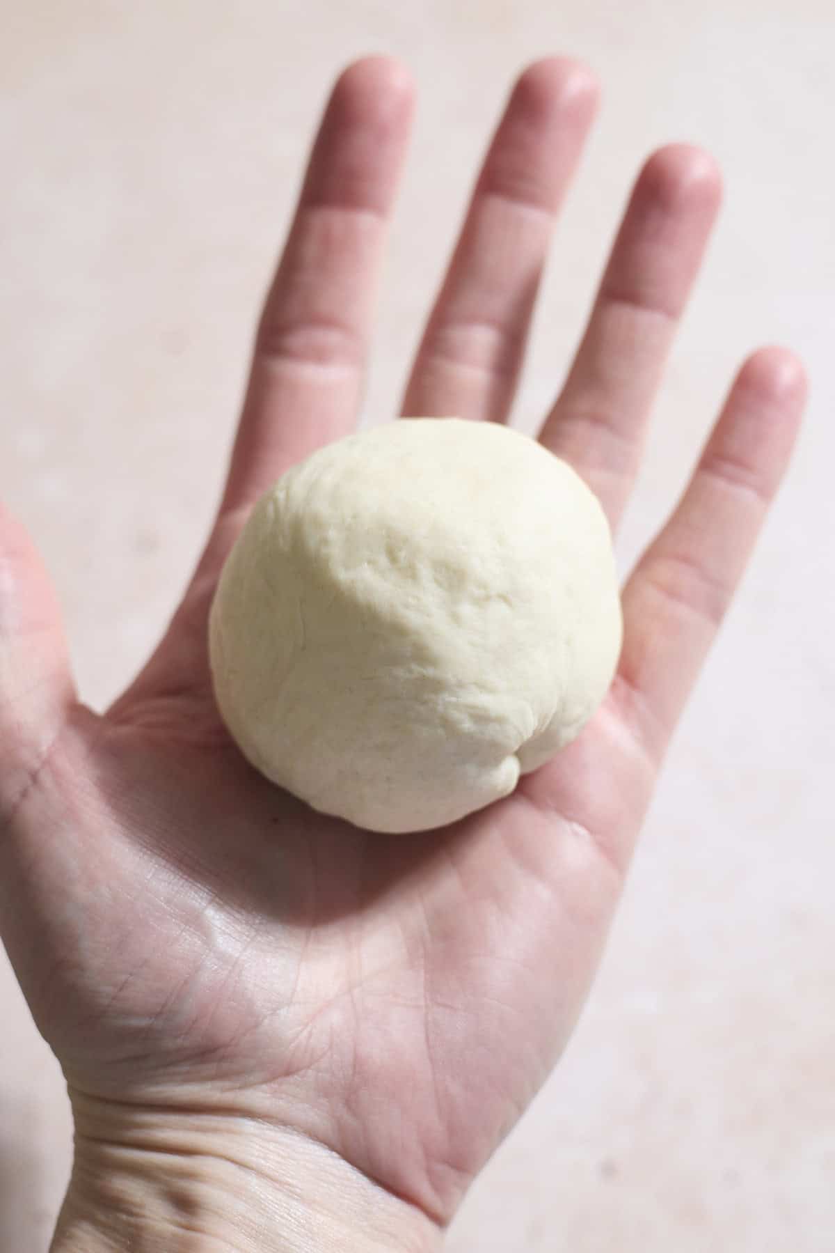 Dough shaped into a ball in the palm of a hand.