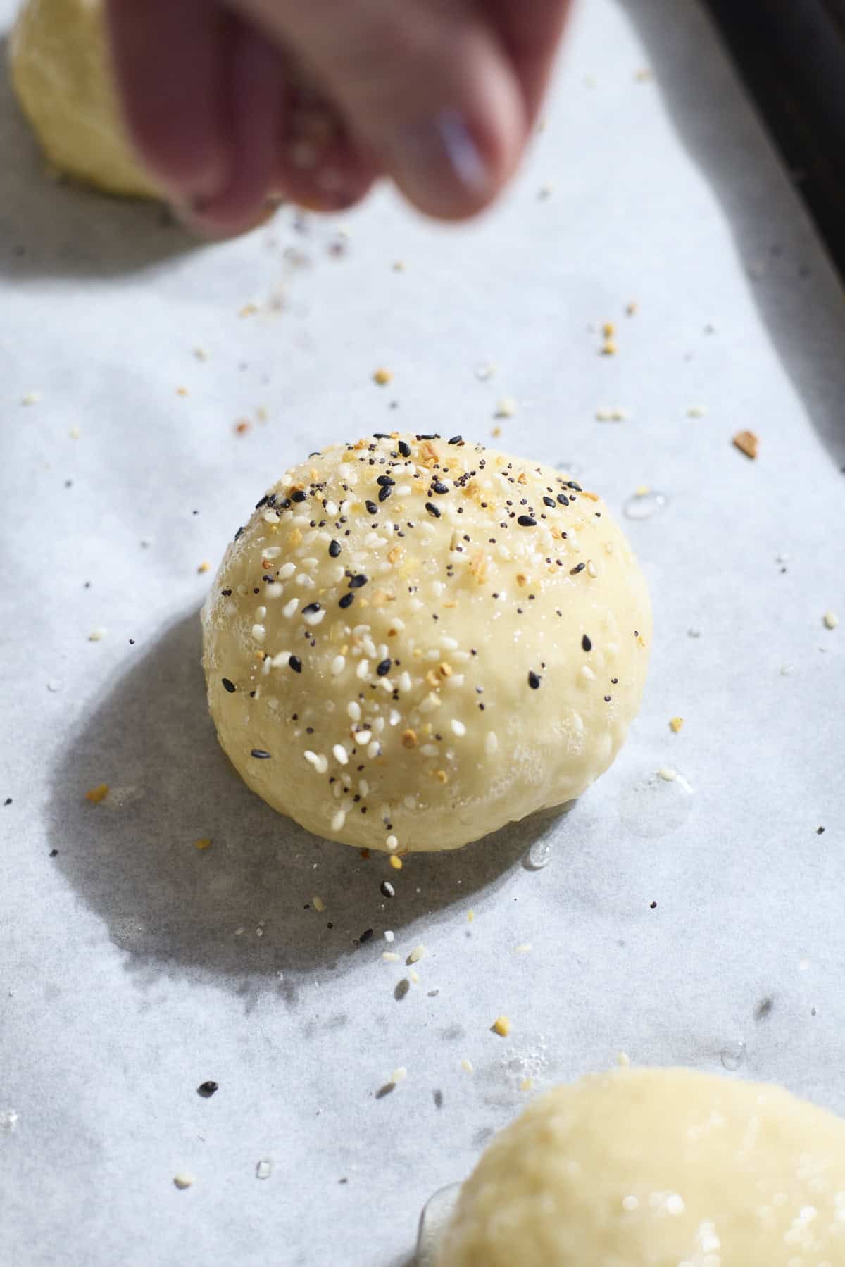 A hand sprinkling toppings on the dough.