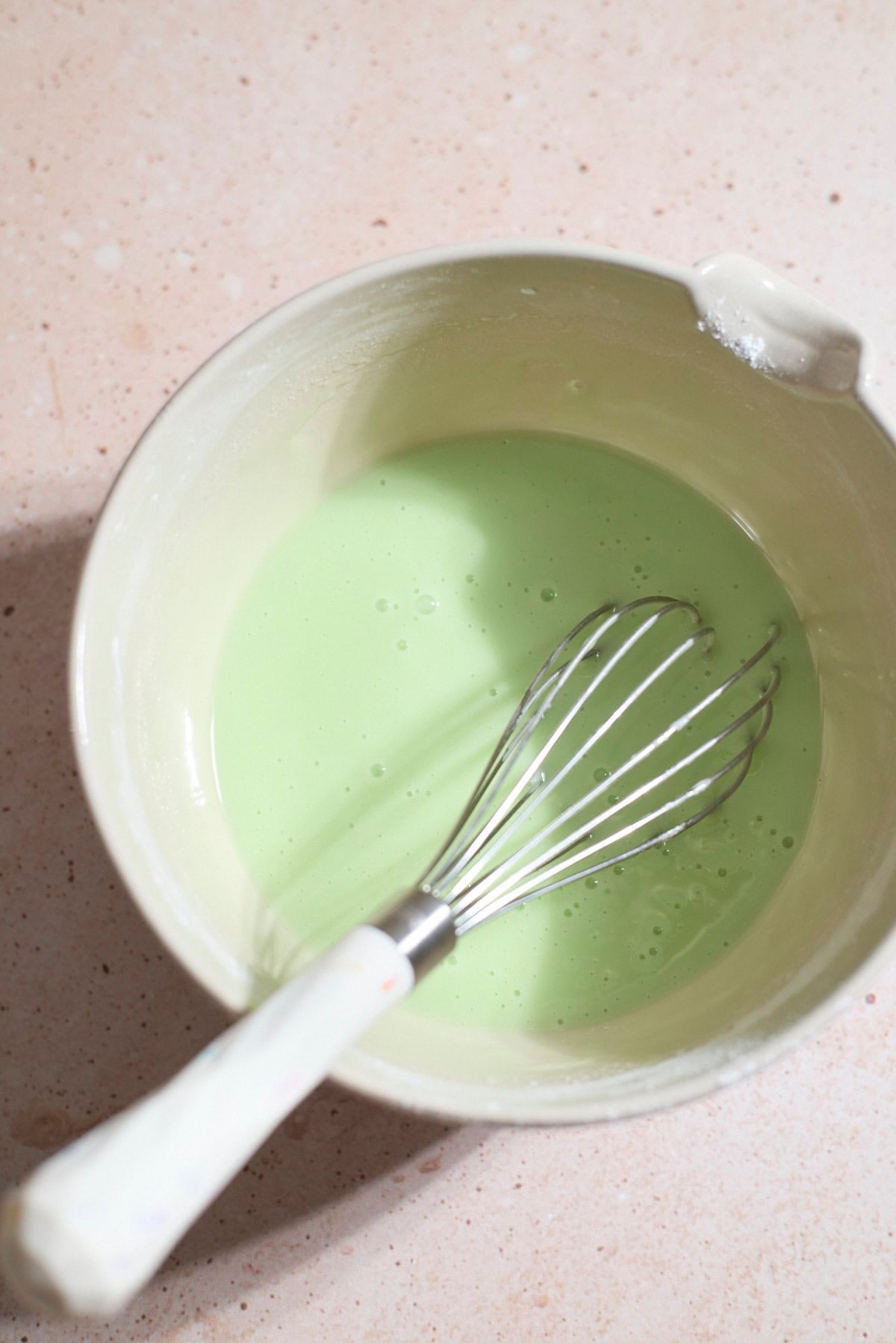 Green icing in a bowl with a whisk.
