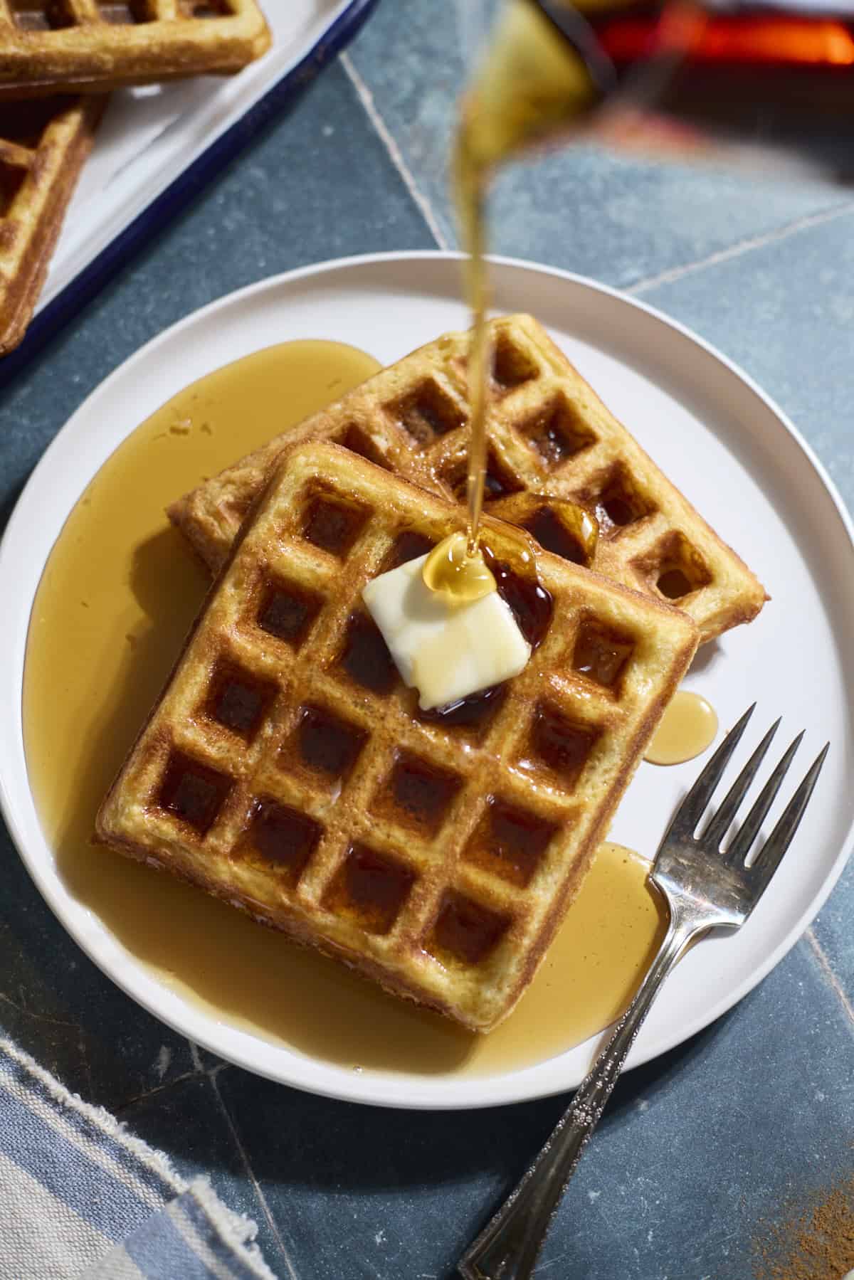 Sourdough Cornmeal Waffles with syrup being poured on top.