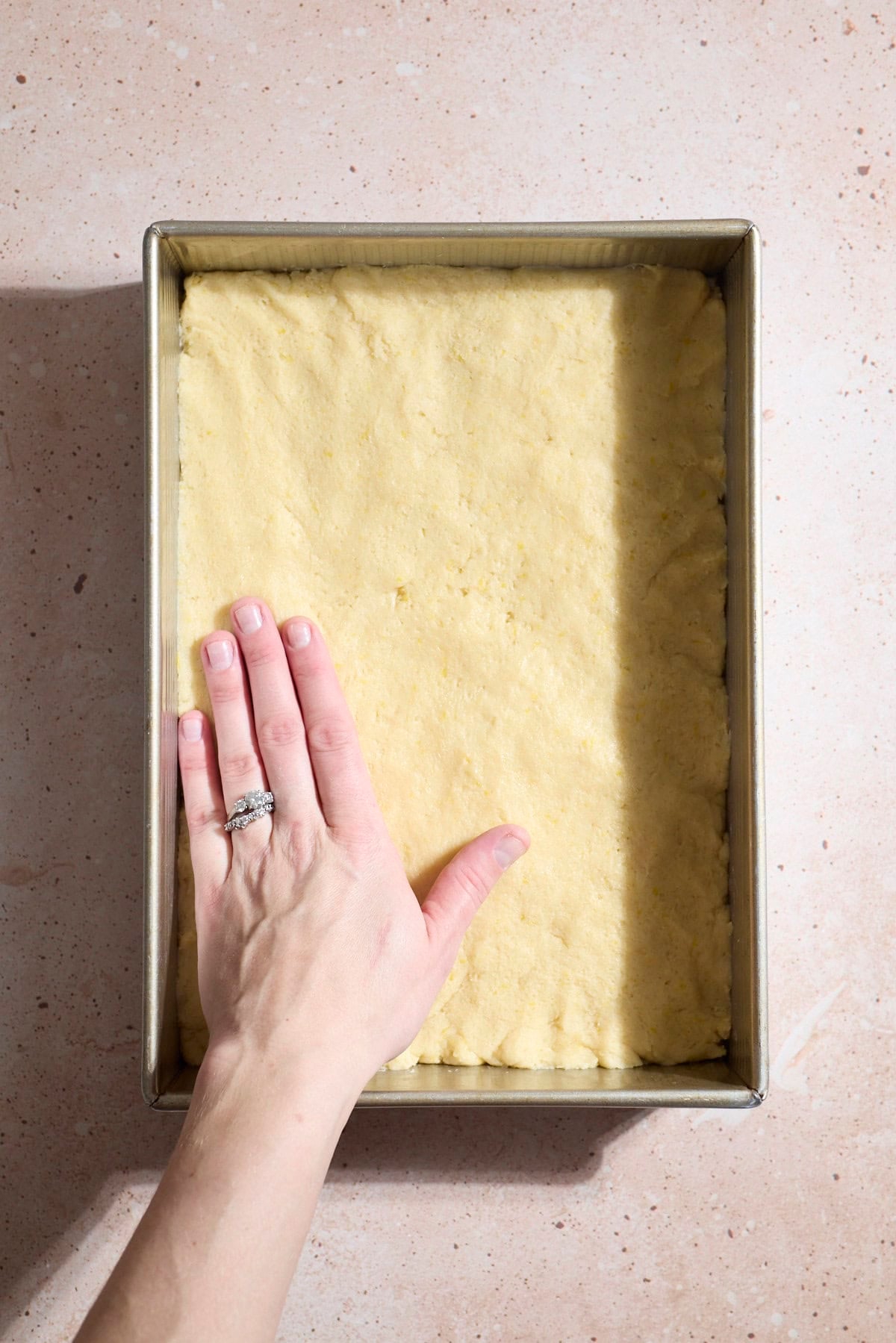 A hand pressing the cookie dough into the pan.