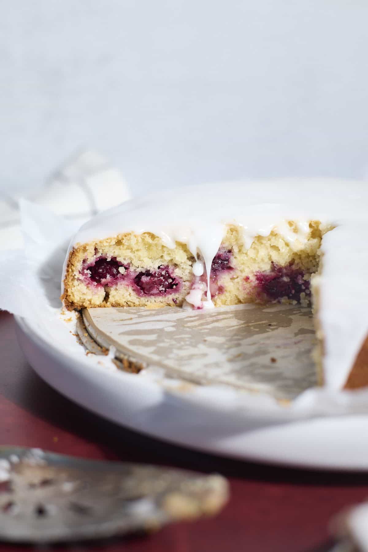 Sourdough Lemon Blackberry Cake with a drip of glaze falling down the side.