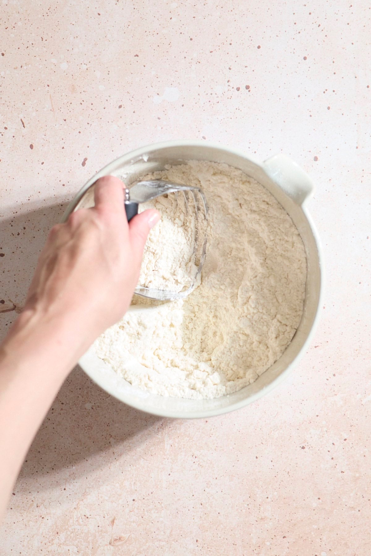 A hand using a pastry cutter in a large bowl.