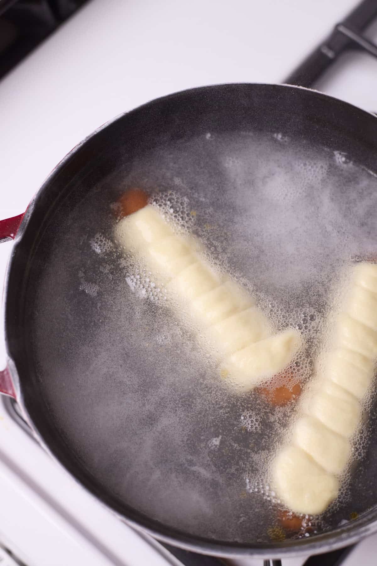 Pretzel-wrapped hot dogs floating in boiling water.
