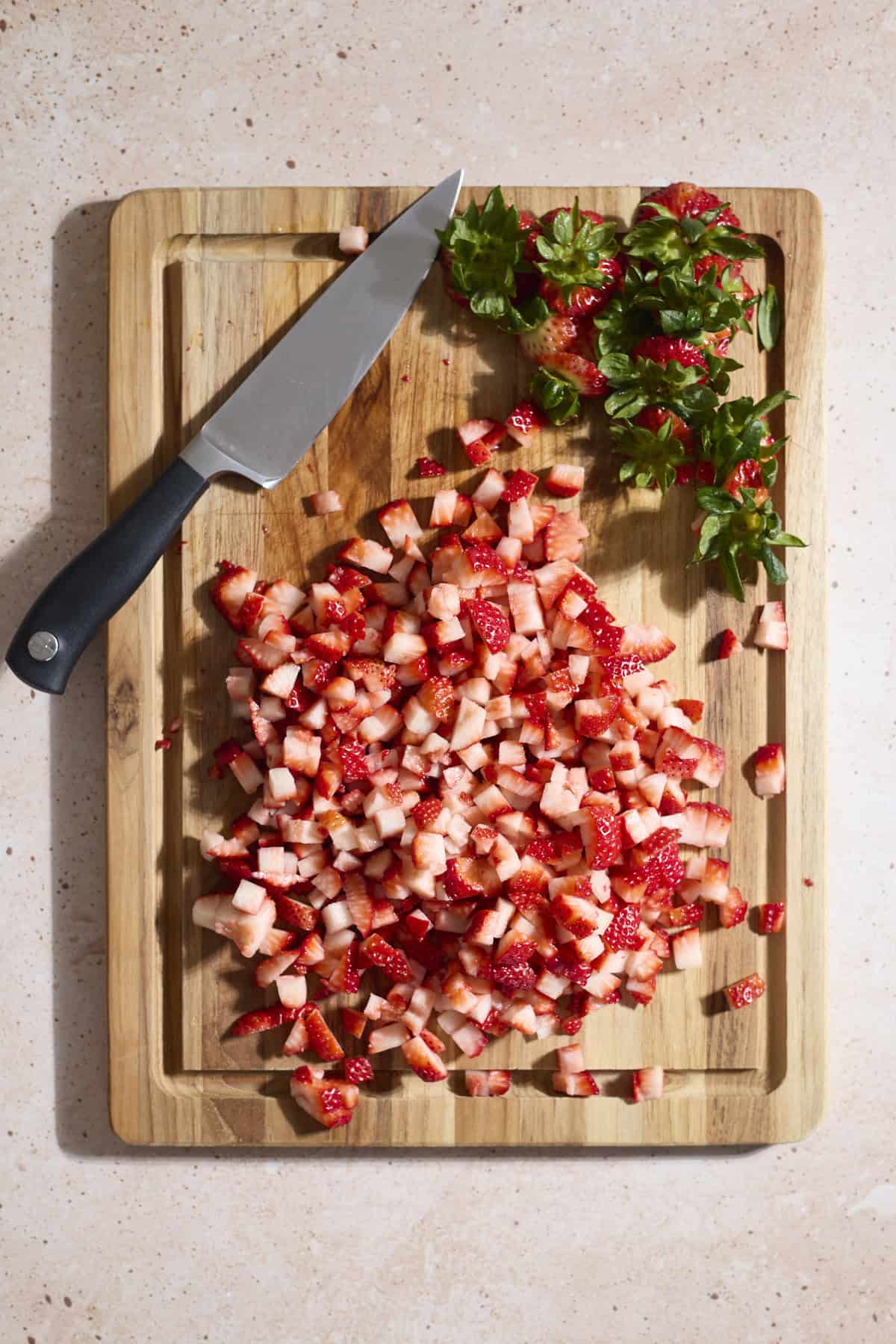 Strawberries diced on a wooden cutting board.