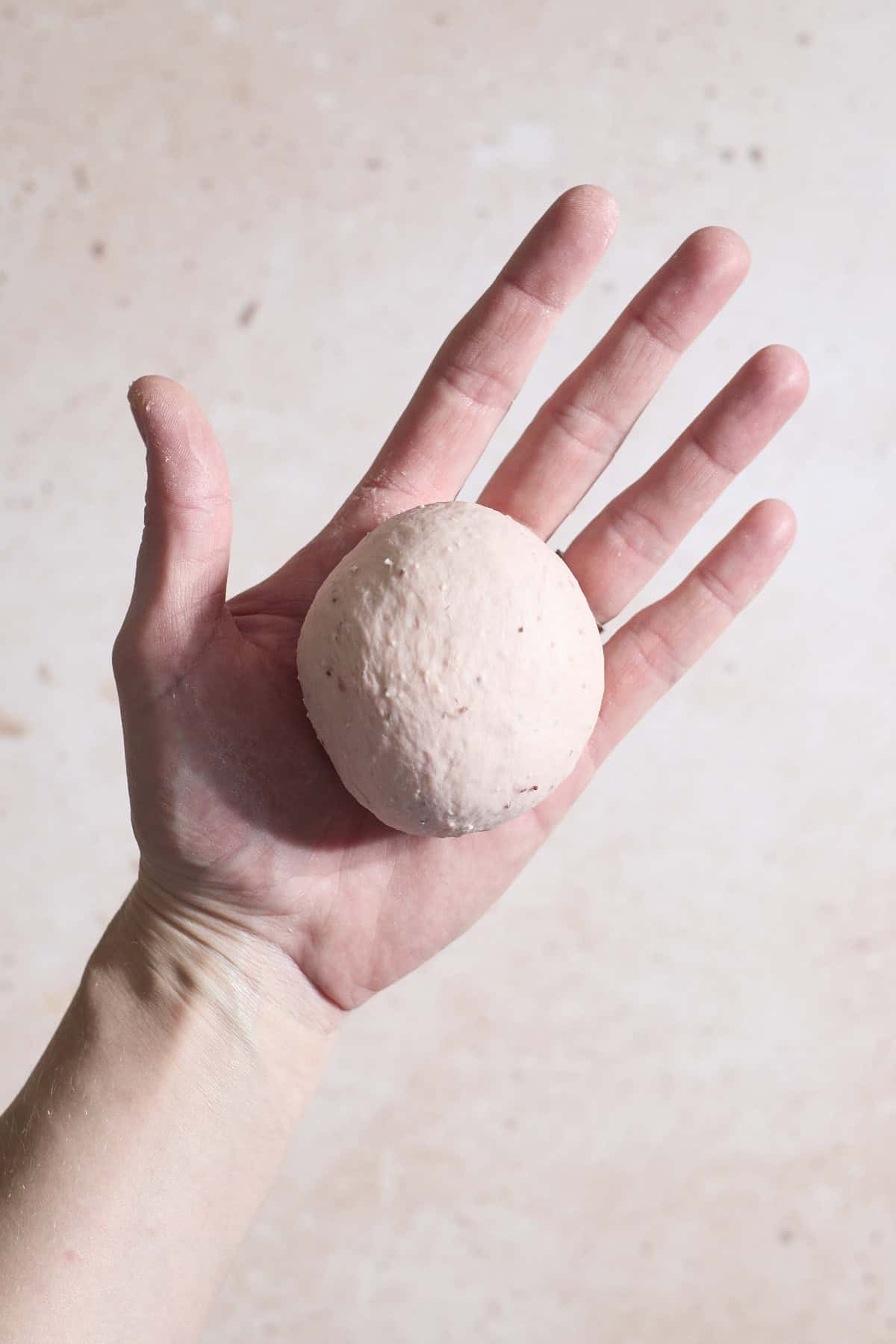 Dough shaped into a ball in the palm of a hand.