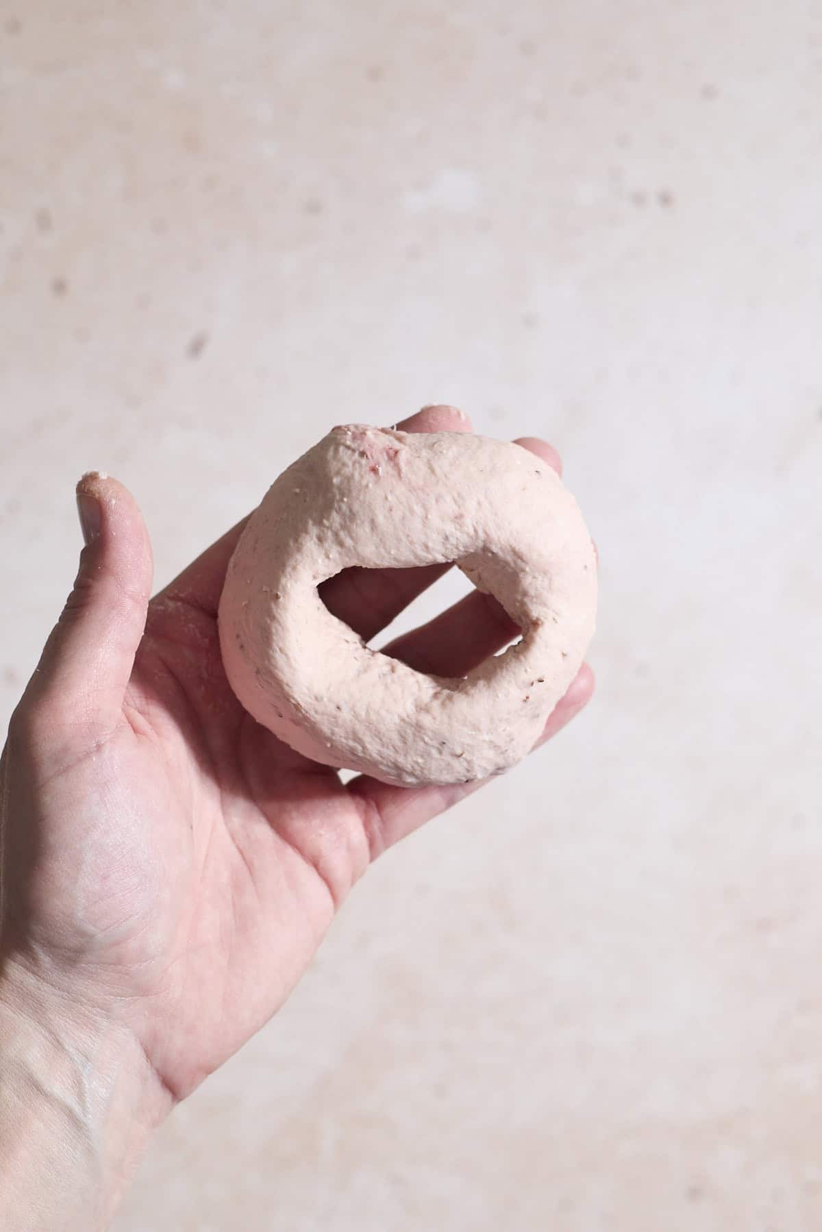 A bagel shaped in the palm of a hand.