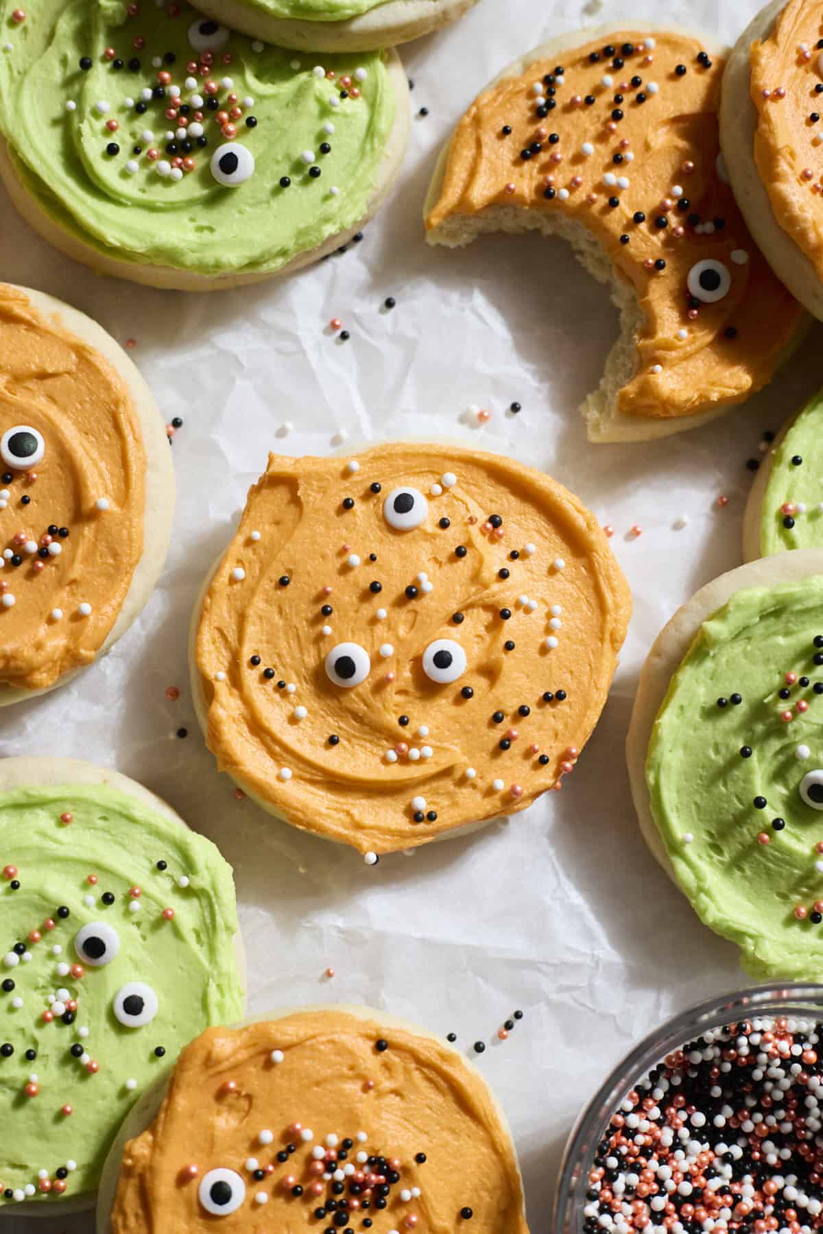 Green and orange frosted cookies with sprinkles on white parchment paper.