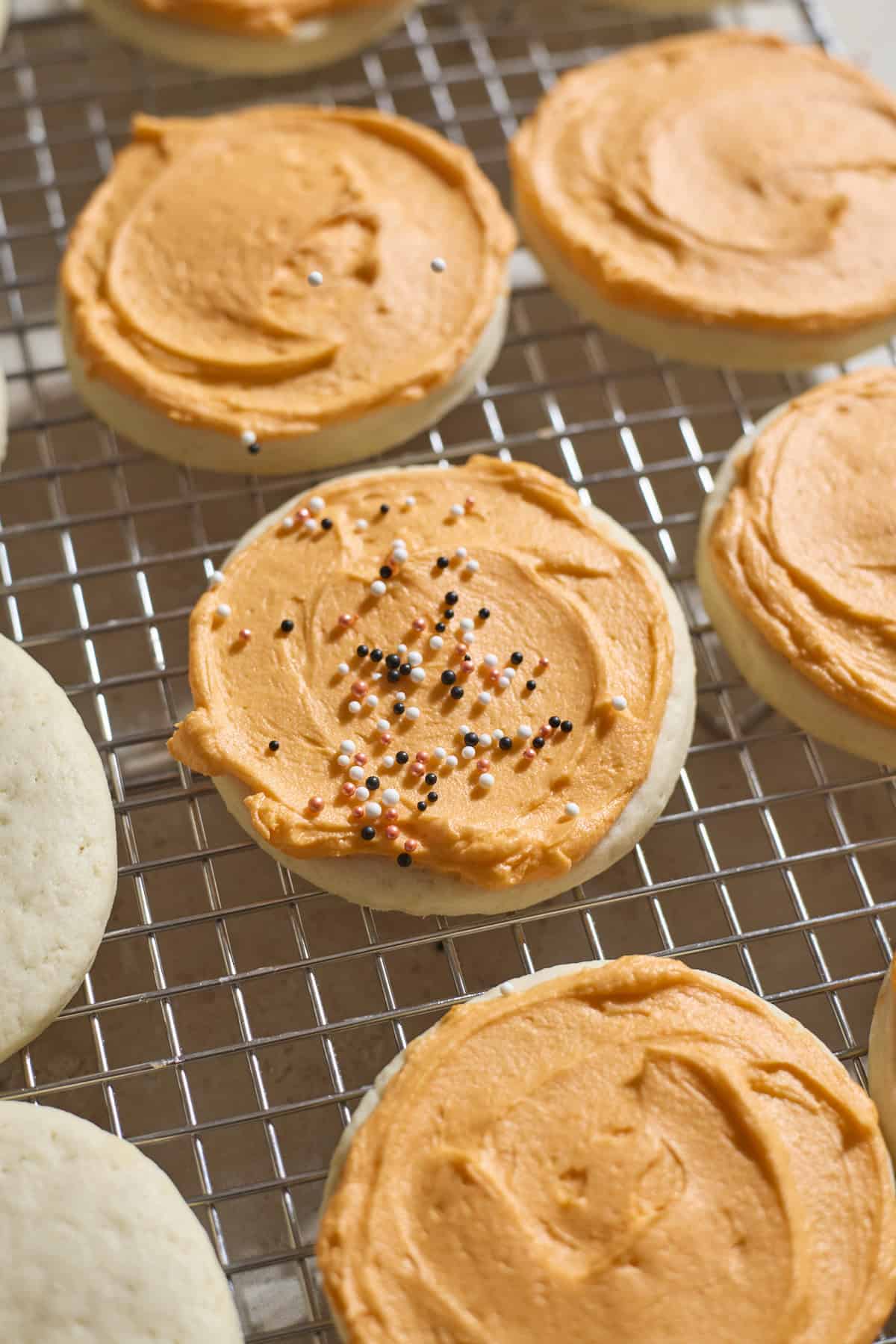 Sprinkles being added to an orange frosted cookie.